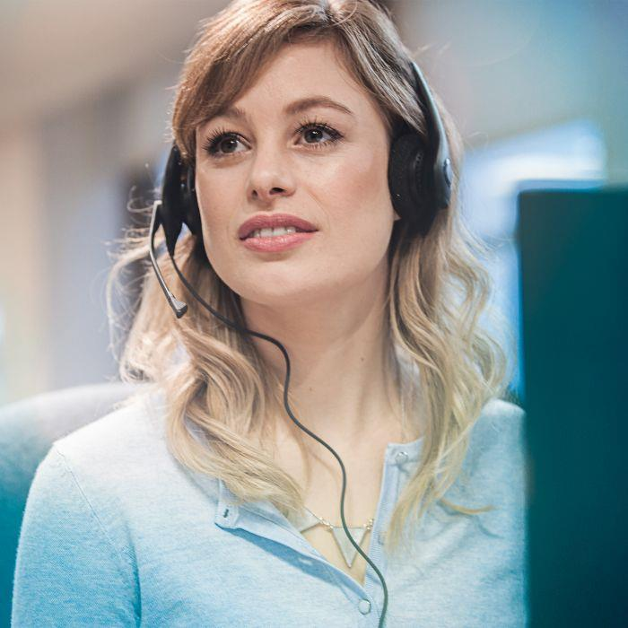 Una representante de servicio al cliente rubia con auriculares y cárdigan azul en una oficina.