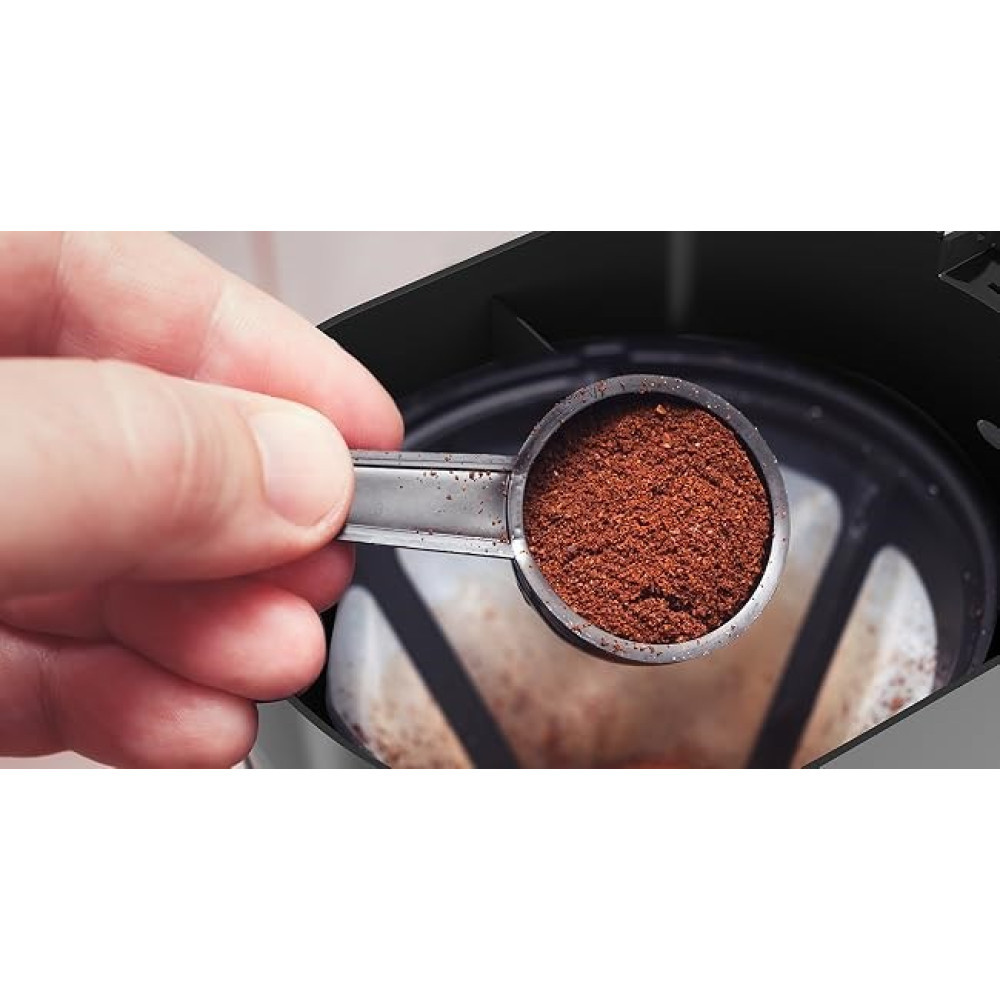 Una mano tiene un cucchiaio nero pieno di caffè macinato sopra un filtro.