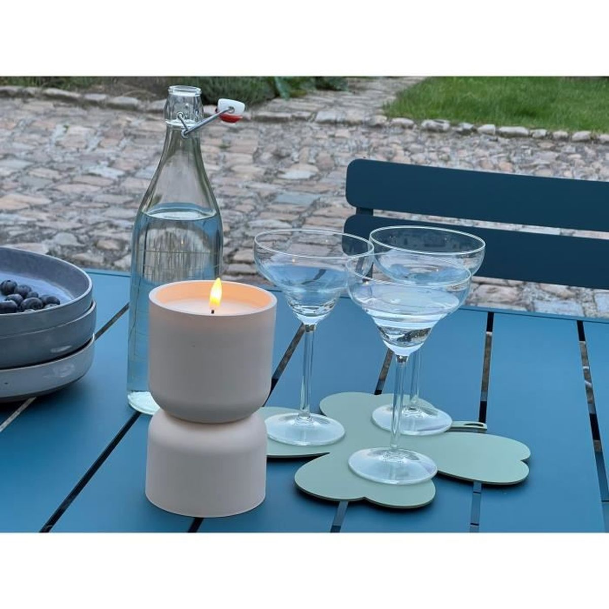 Ein blauer Tisch im Freien mit einer Kerze, drei Gläsern, einer Wasserflasche und einer Schale mit Blaubeeren.