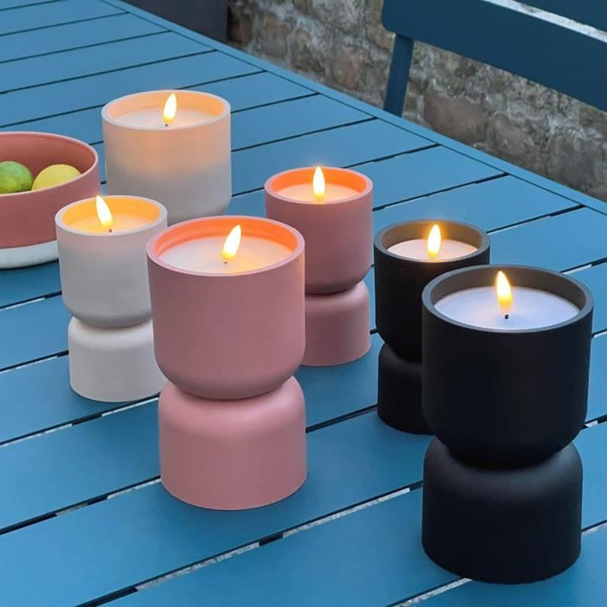 Brennende Kerzen in bunten, doppelstöckigen Kerzenhaltern auf einem blauen Tisch im Freien.