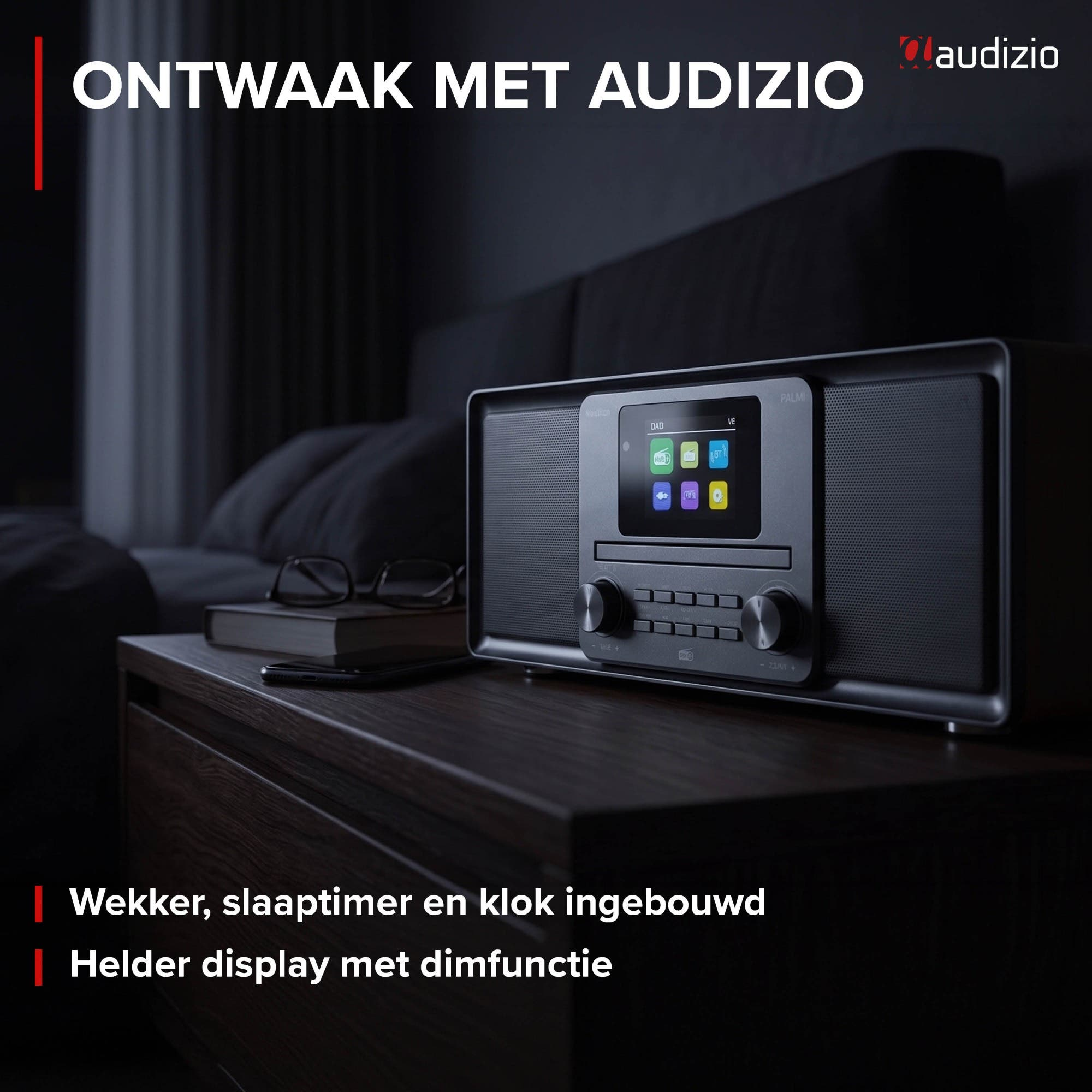 Ein schwarzer Audizio Radiowecker steht auf einem dunklen Nachttisch in einem abgedunkelten Schlafzimmer.