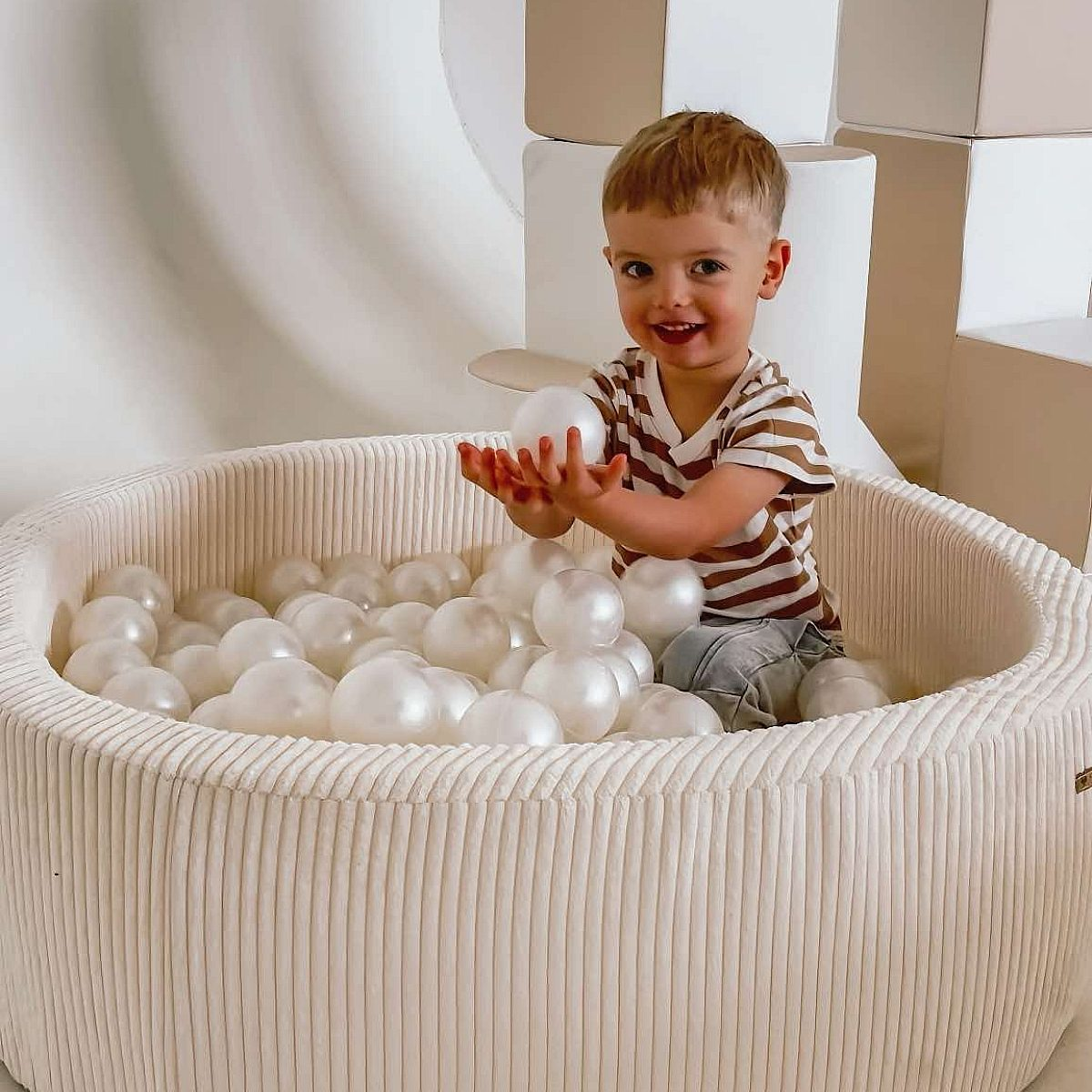Kleiner Junge sitzt im Bällebad und hält einen weißen Ball.