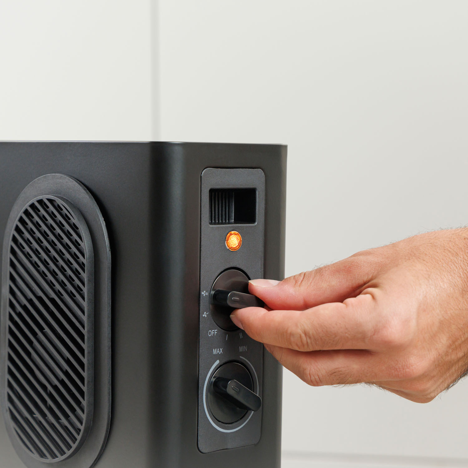 Ręka przekręca pokrętło czarnej nagrzewnicy elektrycznej.