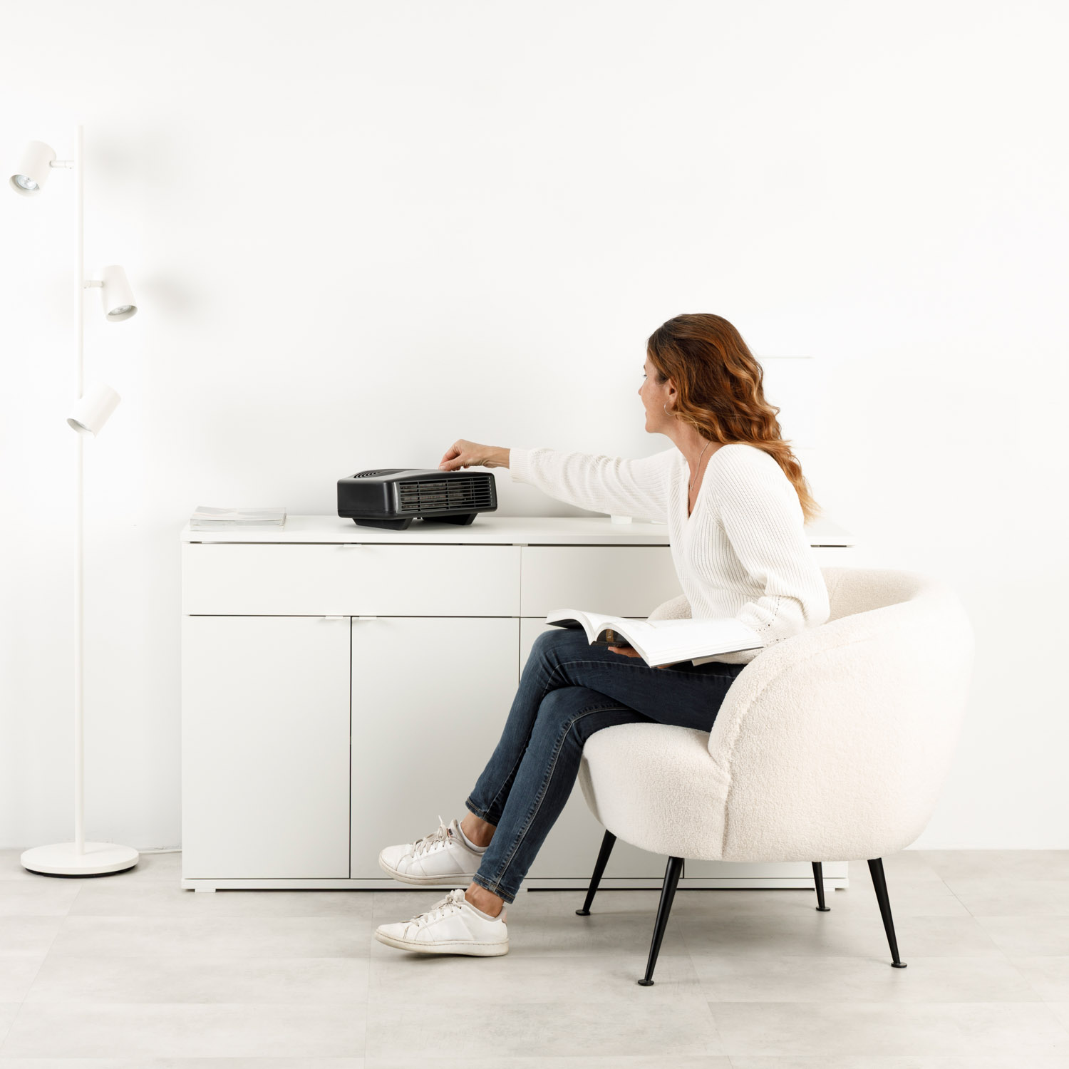 Kobieta w białym fotelu naciska przycisk grzejnika na białej szafce.