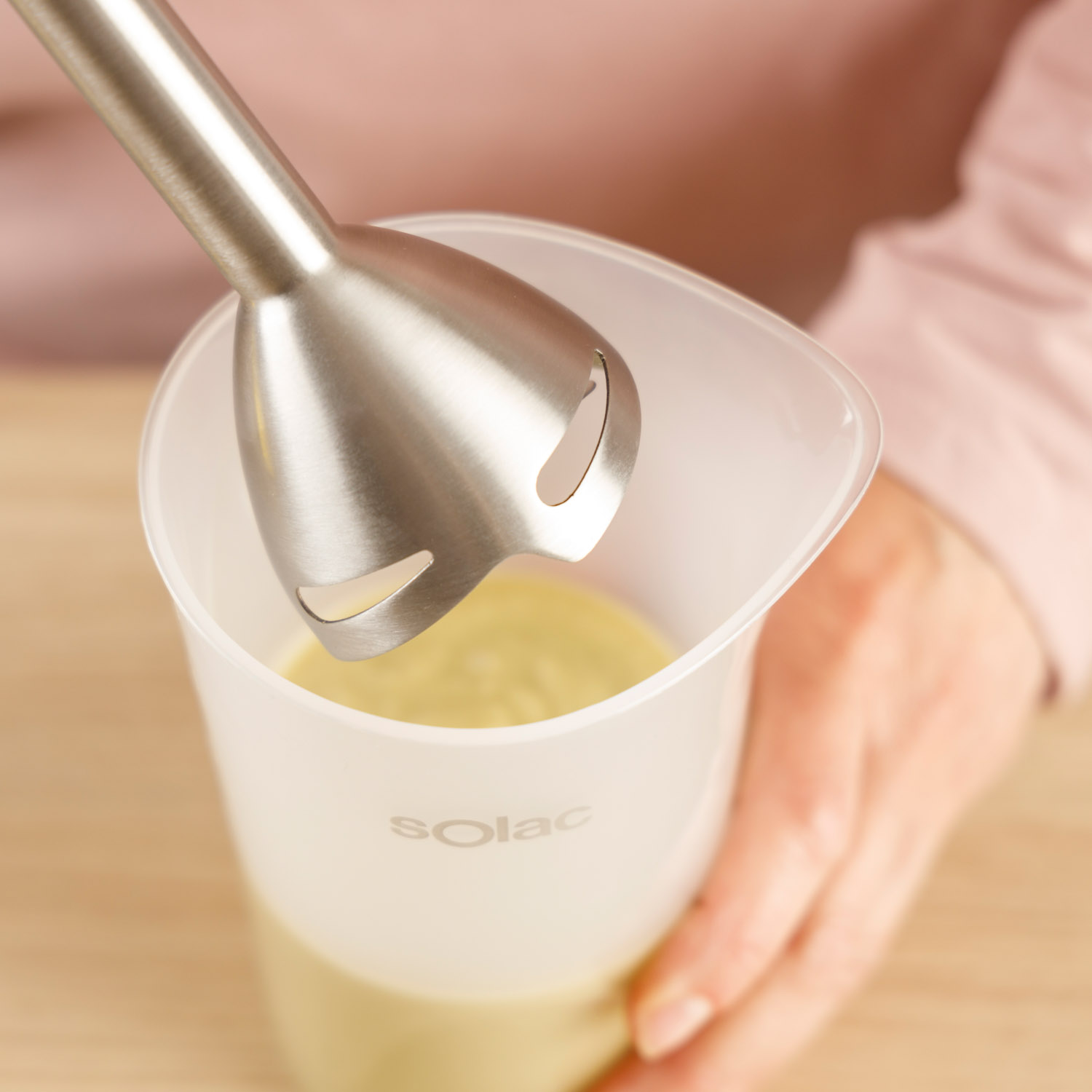 Blender ręczny ze stali nierdzewnej nad miarką z żółtym płynem.