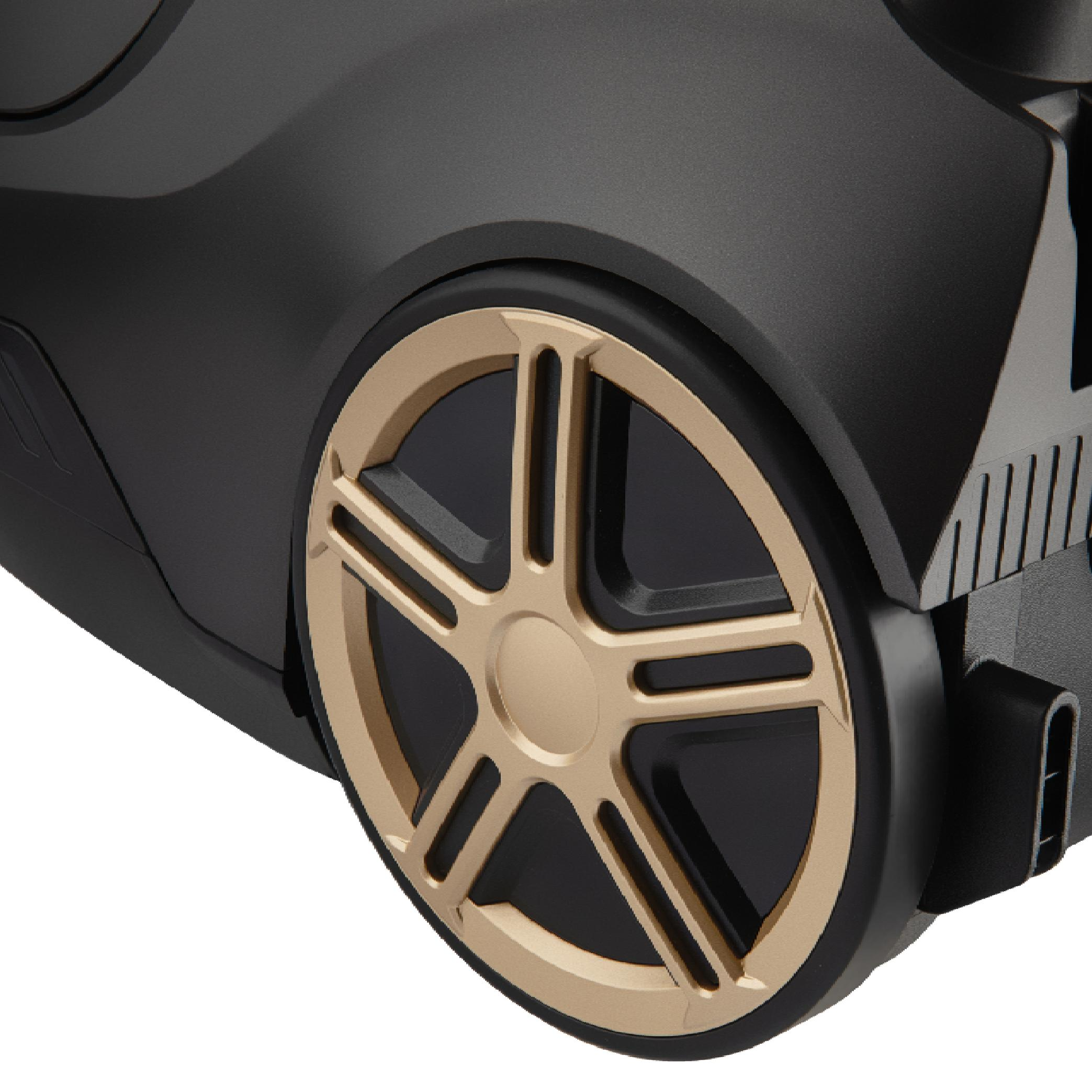 Close-up of a large matte black vacuum cleaner body featuring a stylish gold-accented wheel.