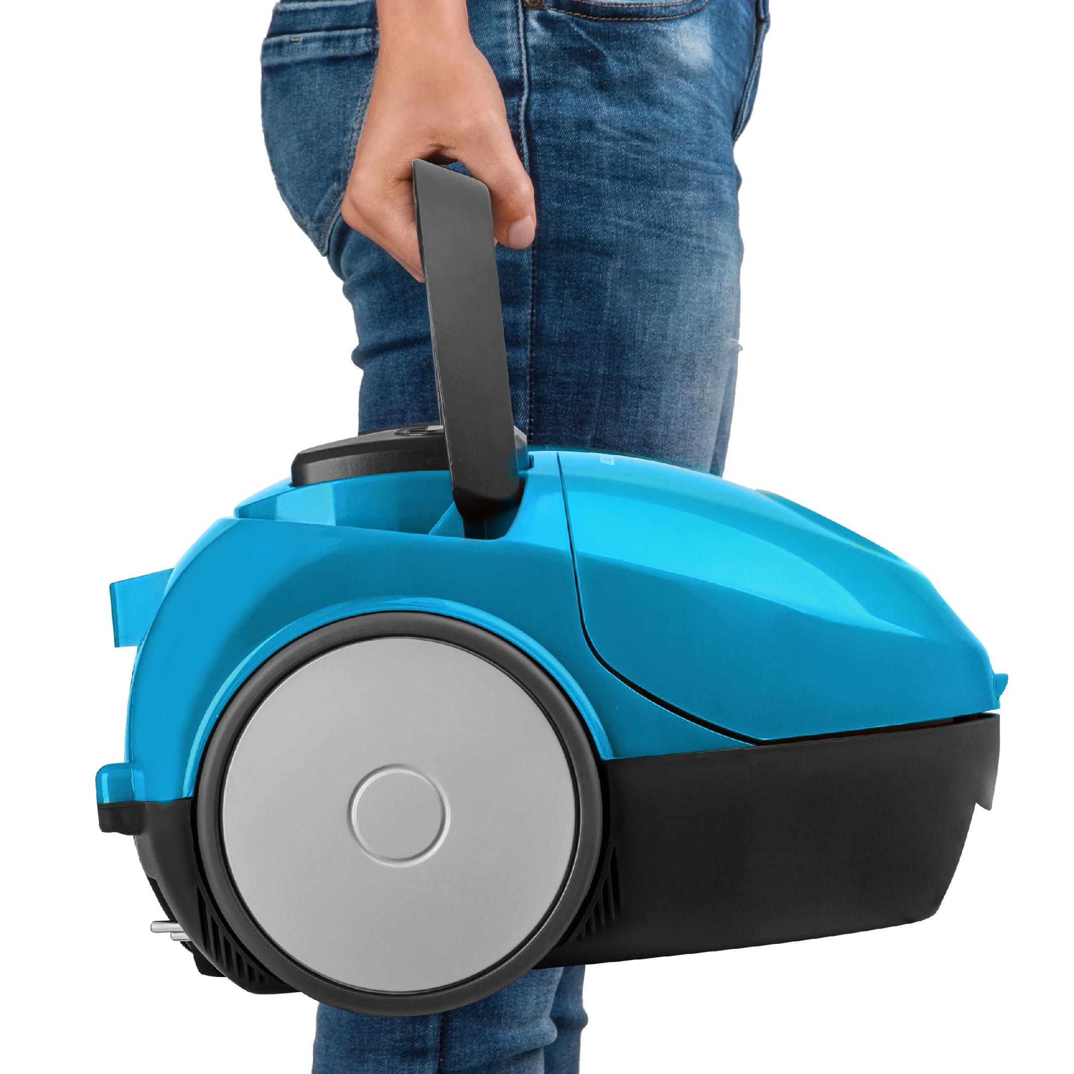 Una persona con jeans azules sostiene una aspiradora de bote azul y negro por el asa.