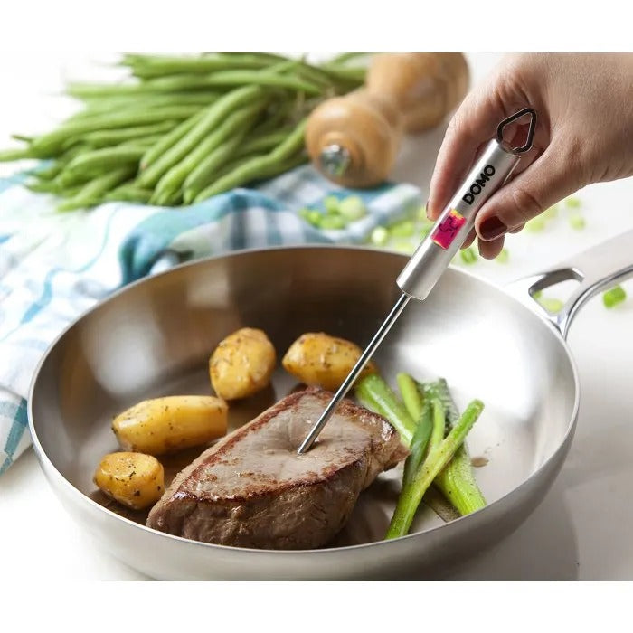 Mano mide la temperatura de la carne con un termómetro en una sartén con patatas y judías.