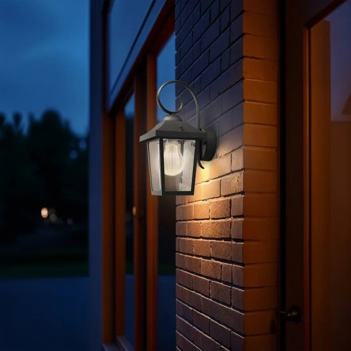 Un farol de pared negro ilumina una pared de ladrillo rojo al atardecer.