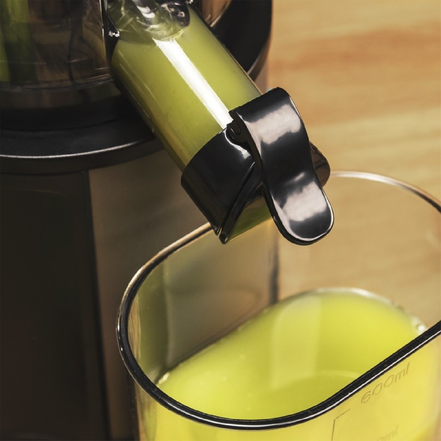 Succo verde scorre da un estrattore in un bicchiere su un tavolo di legno.