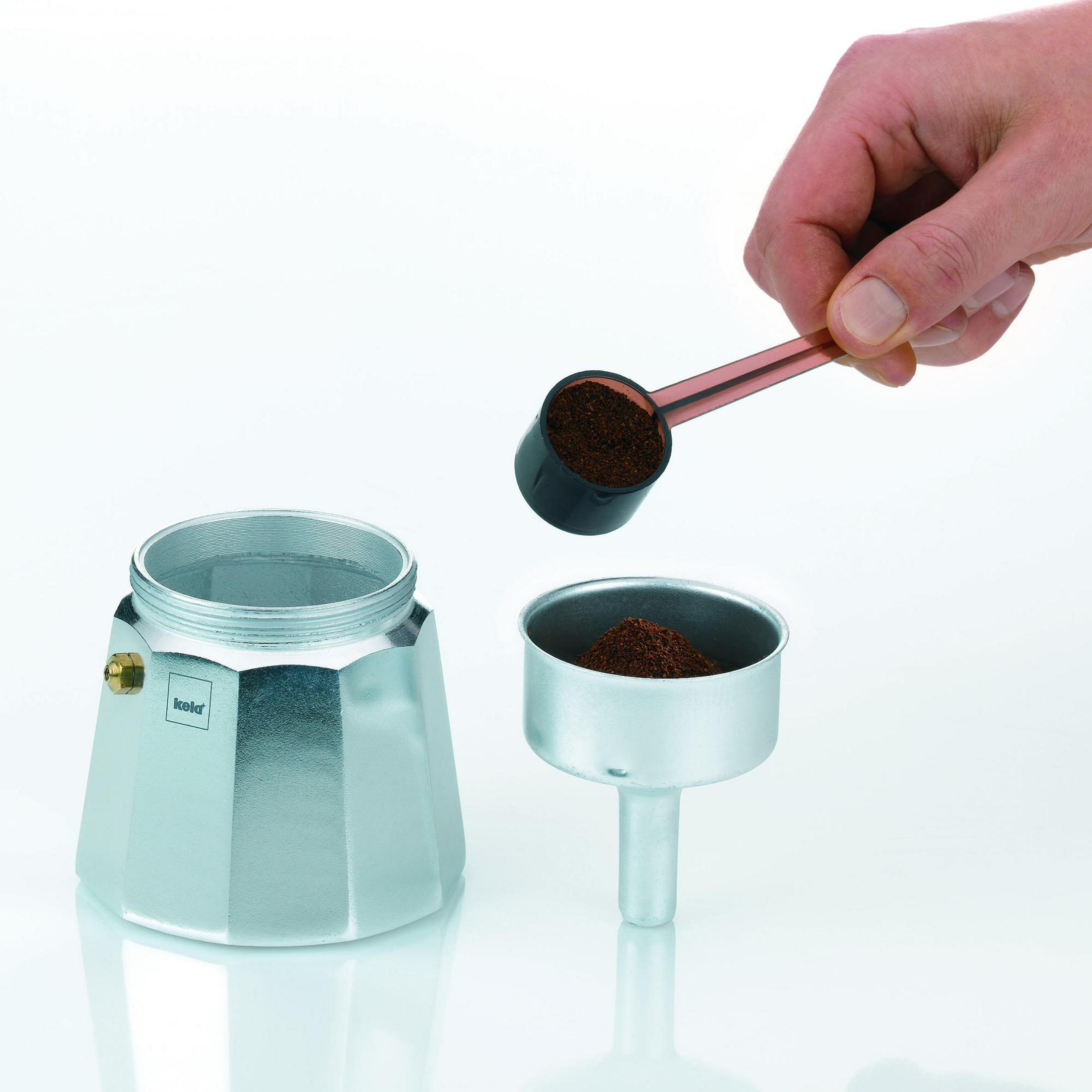 Une main verse du café moulu d'une cuillère dans le filtre d'une cafetière argentée.