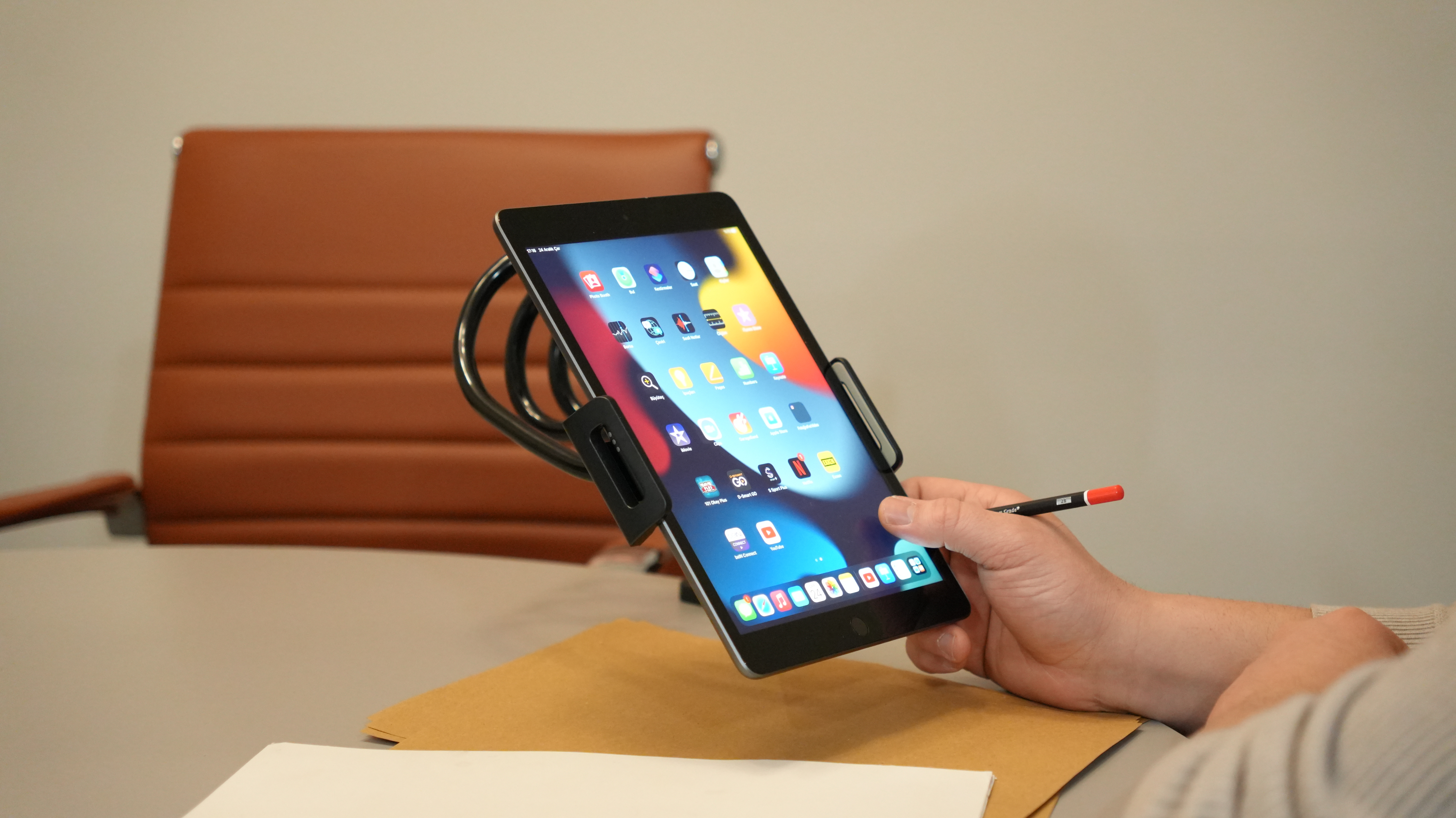 Masada esnek bir tutucuda duran bir tablet ve yakınında kalem tutan bir el.