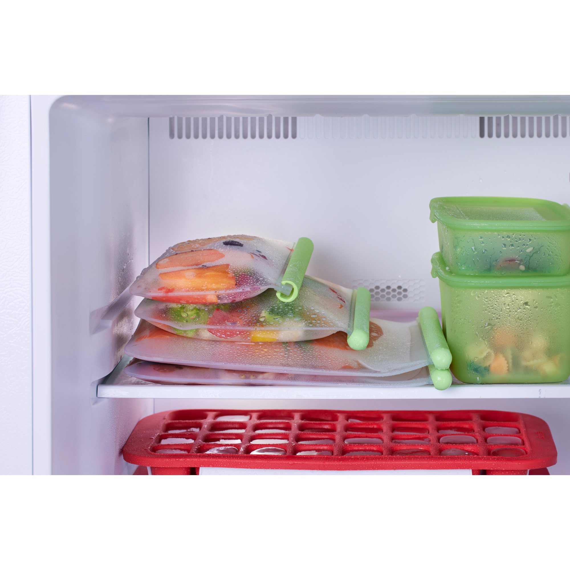 Im Kühlschrank liegen versiegelte Beutel mit Lebensmitteln und grüne Behälter über einer roten Eiswürfelform.