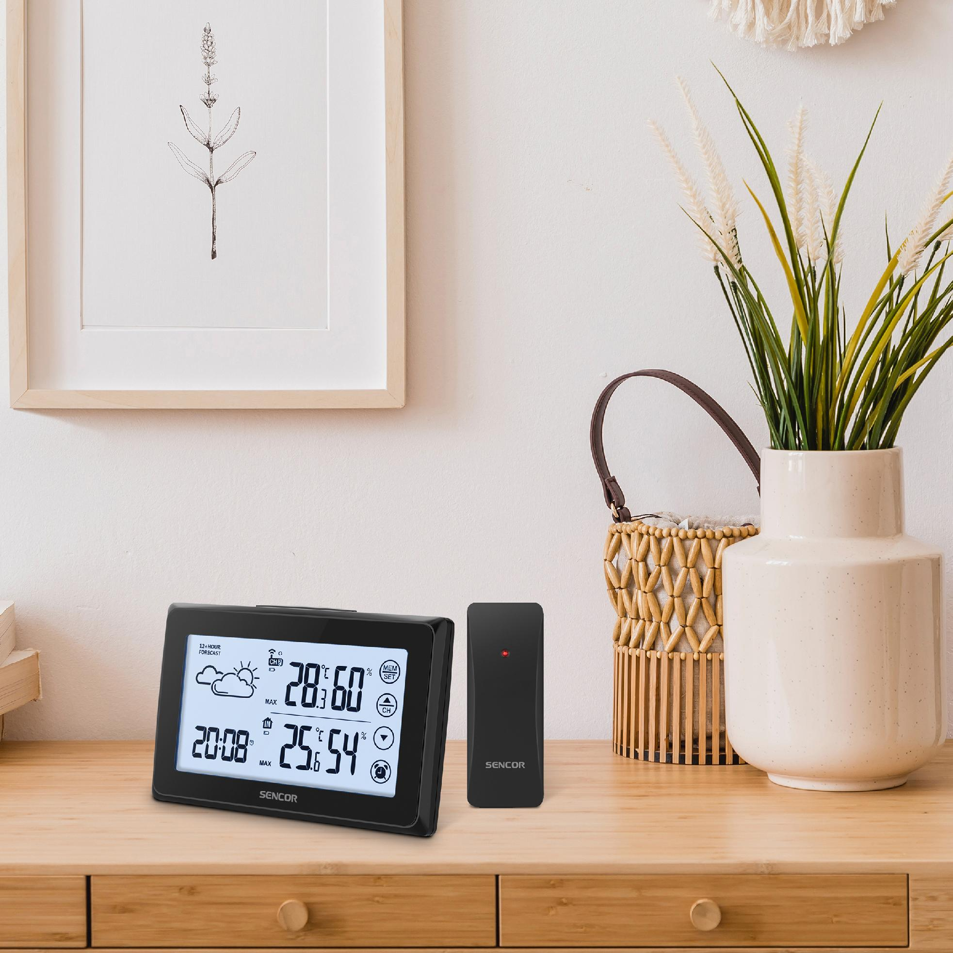 Wetterstation mit Display und Sender auf Holztisch vor weißer Wand mit Bild.