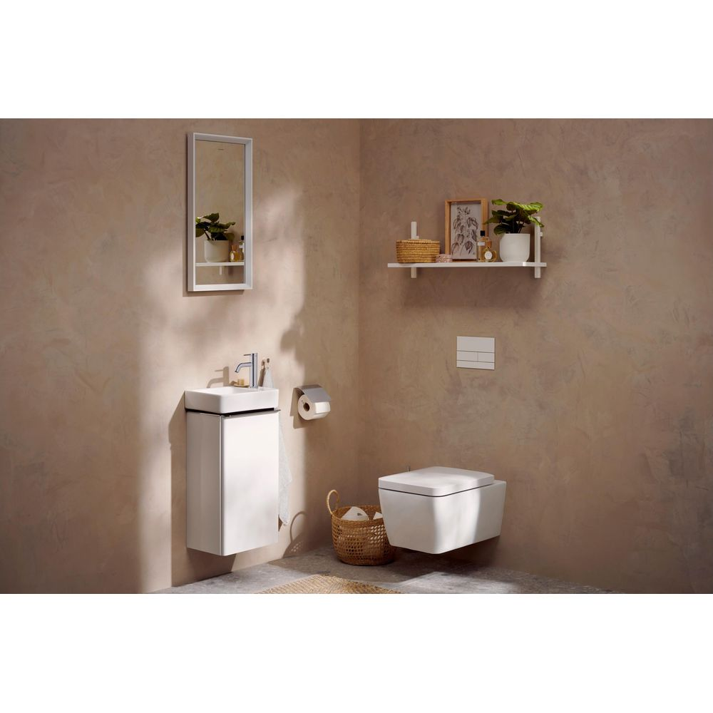 Ein modernes Badezimmer hat ein weißes Hänge-WC, Waschtisch, Spiegel und ein Wandregal mit Pflanzen.