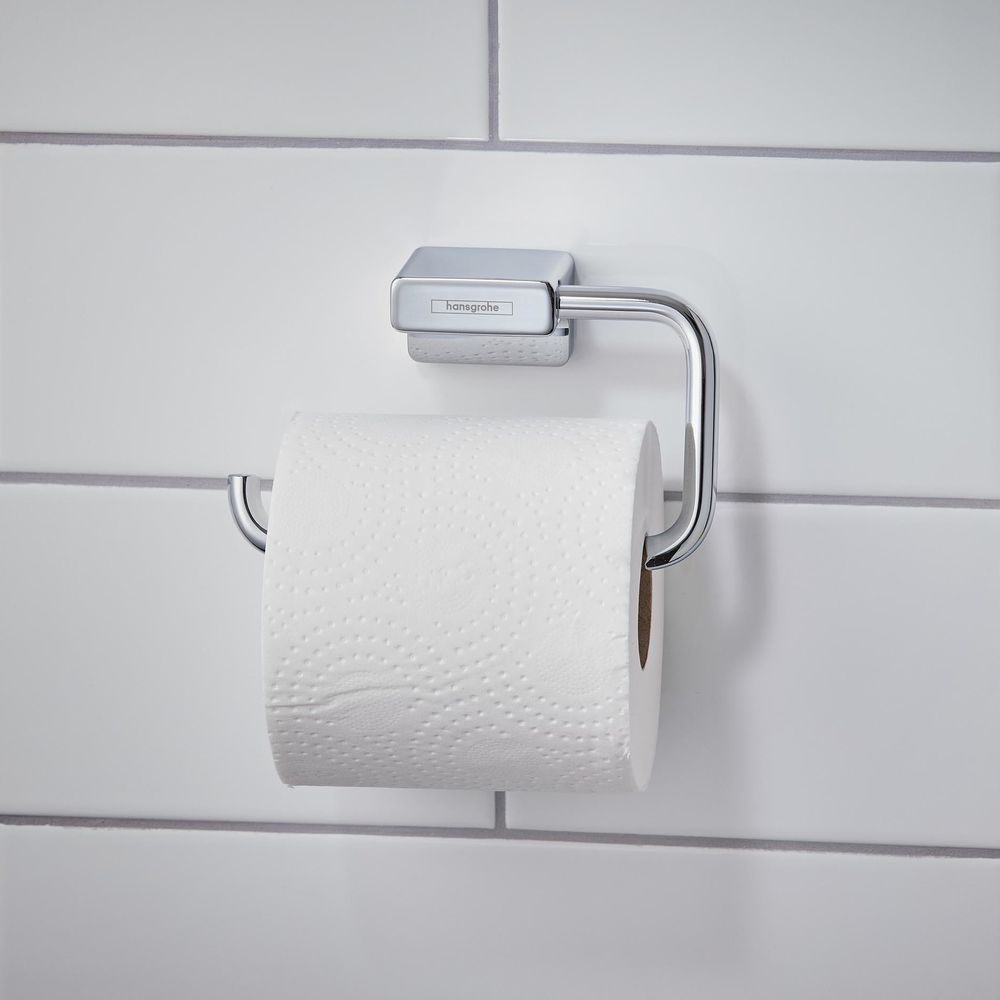Ein glänzender, verchromter Toilettenpapierhalter mit einer weißen Rolle Toilettenpapier vor weißen Fliesen.