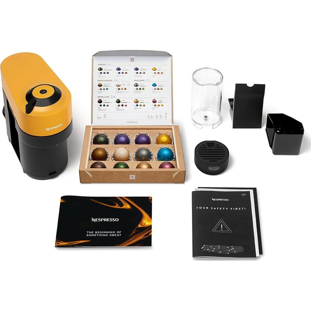 Cafetière Nespresso jaune et noire avec capsules, accessoires et manuels sur fond blanc.
