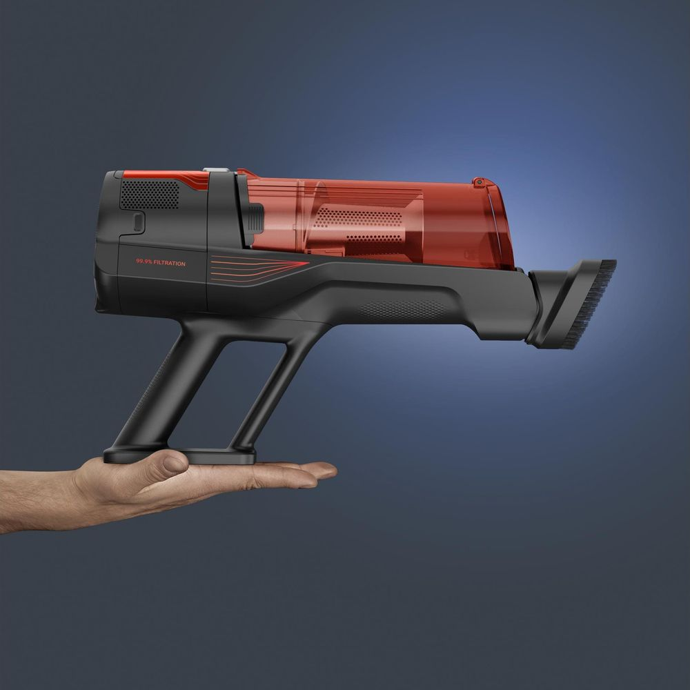 Una mano regge un moderno aspirapolvere portatile nero con serbatoio della polvere rosso su sfondo blu.