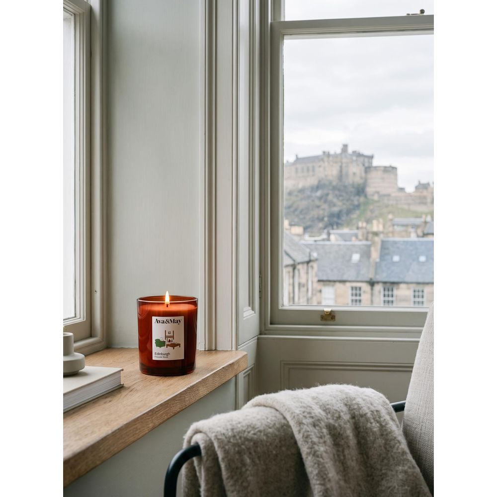 Una candela accesa sul davanzale con un libro, vista di un castello dalla finestra e coperta su una sedia.