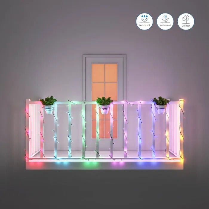 Una barandilla de balcón blanca con luces de colores y tres macetas frente a una ventana iluminada.