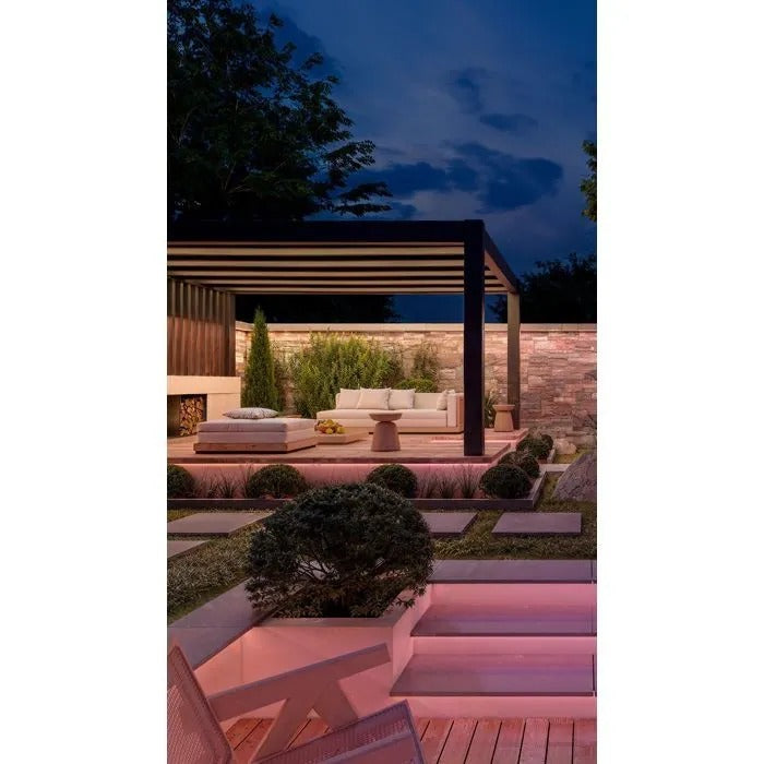 Moderno patio illuminato al crepuscolo con divano, pergola, muro in pietra e gradini da giardino.