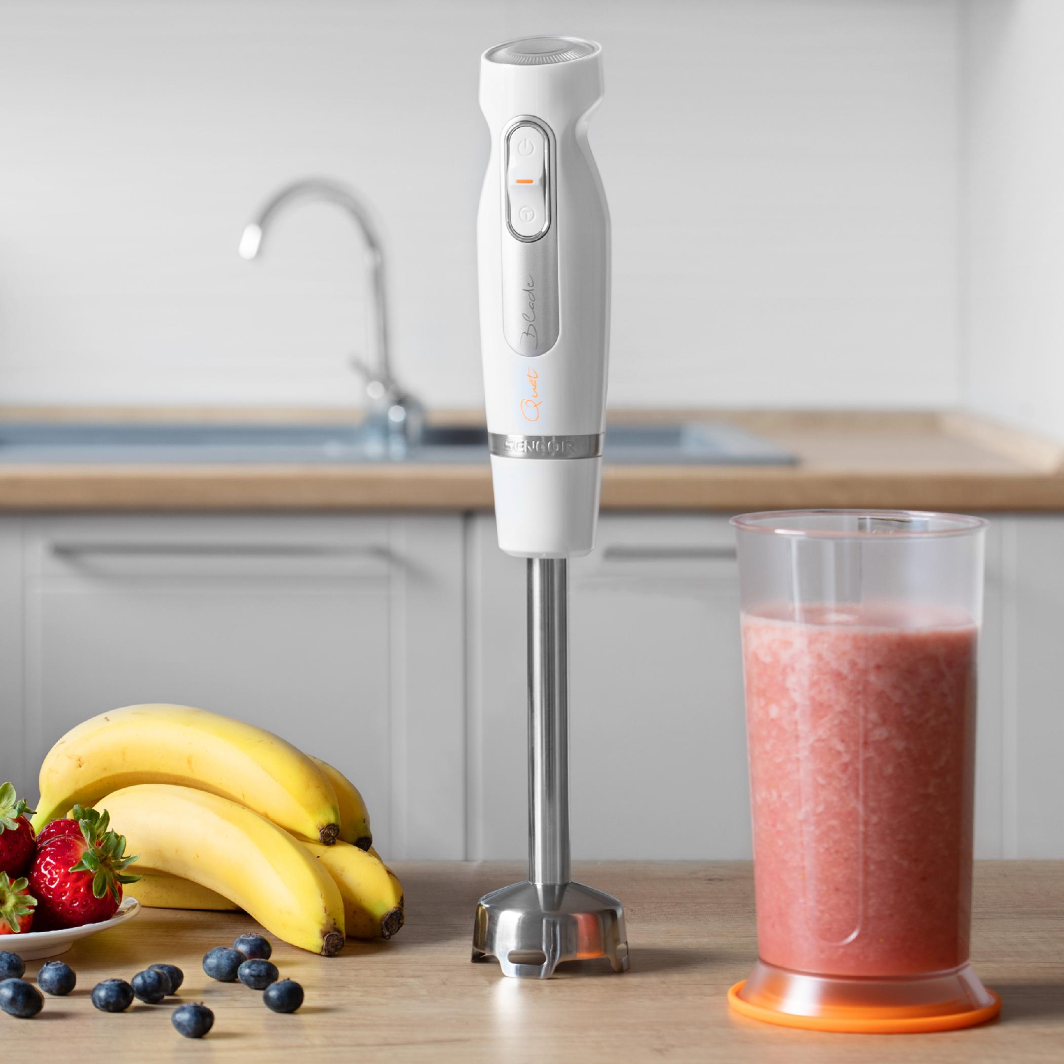 Biały blender ręczny na drewnianym stole z bananami, truskawkami, jagodami i smoothie.