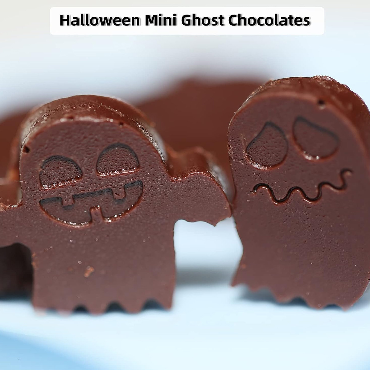 Zwei kleine Halloween-Schokoladengespenster mit lustigen Gesichtern stehen auf einem blauen Tisch.