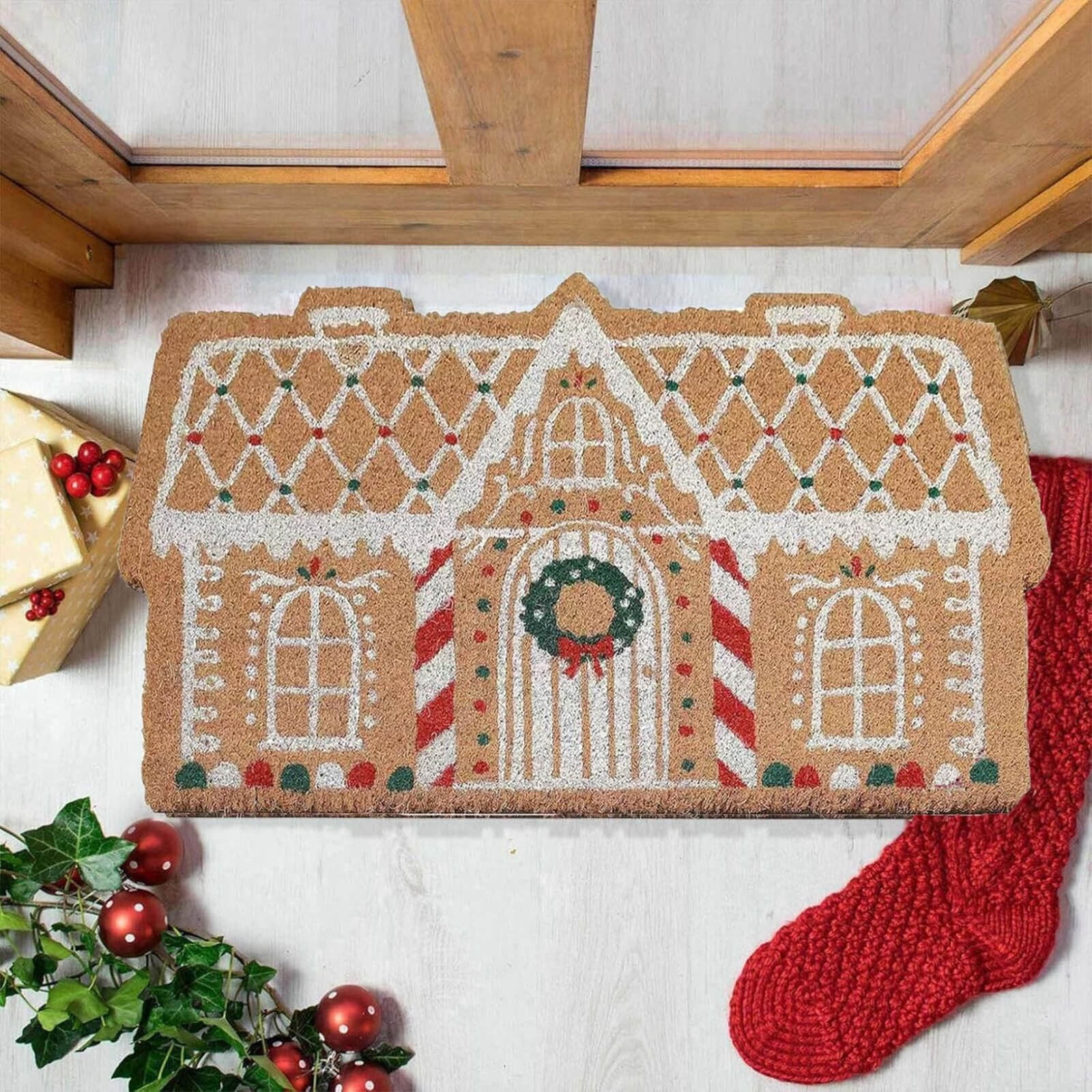 Eine weihnachtliche Lebkuchenhaus-Fußmatte mit weißem Zuckerguss, Kranz, Geschenken und einem roten Strumpf.