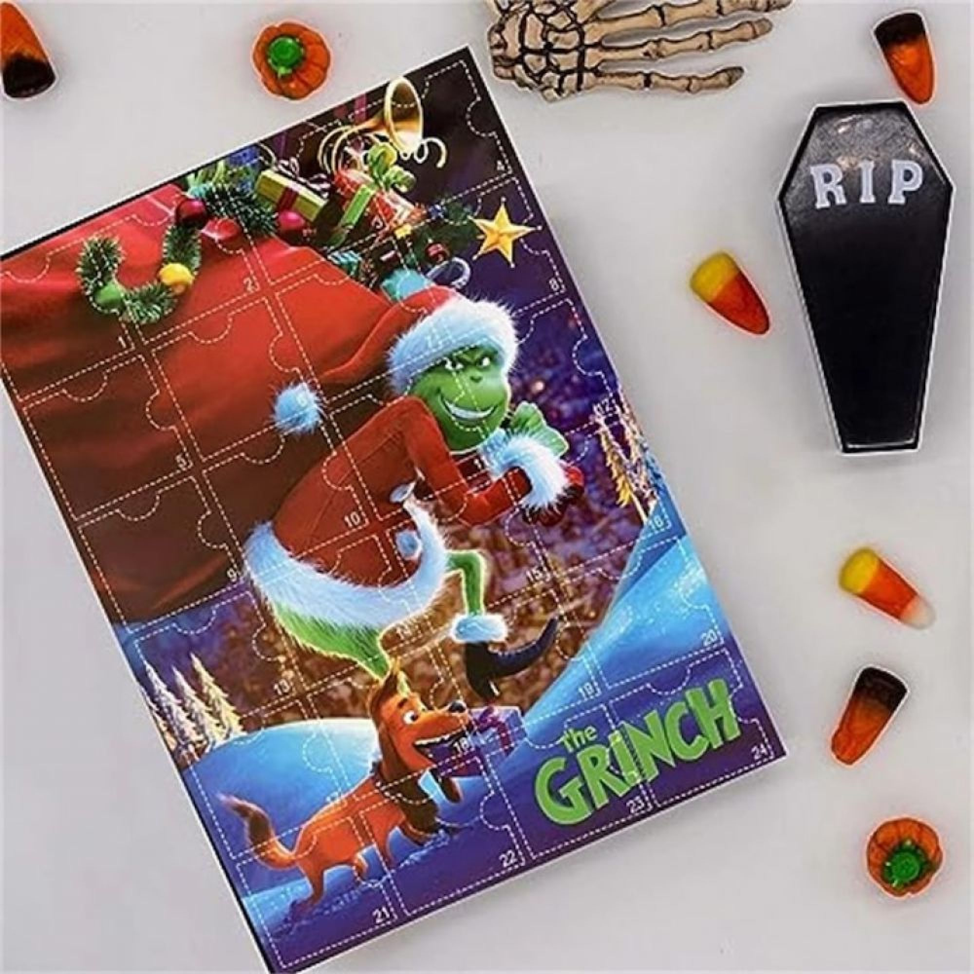 Ein Grinch Adventskalender-Puzzle liegt auf einer weißen Oberfläche mit Halloween-Süßigkeiten und Sarg-Dekor.