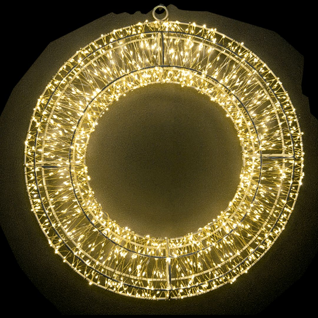 Una corona de metal redonda y colgante iluminada con luces de hadas blancas cálidas sobre un fondo oscuro.