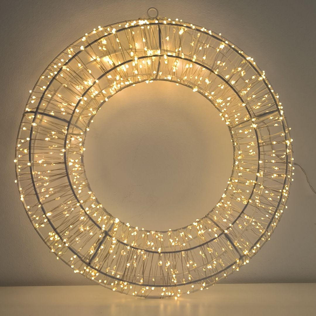 Un marco de metal circular decorado con muchas luces LED de color blanco cálido cuelga contra una pared clara.