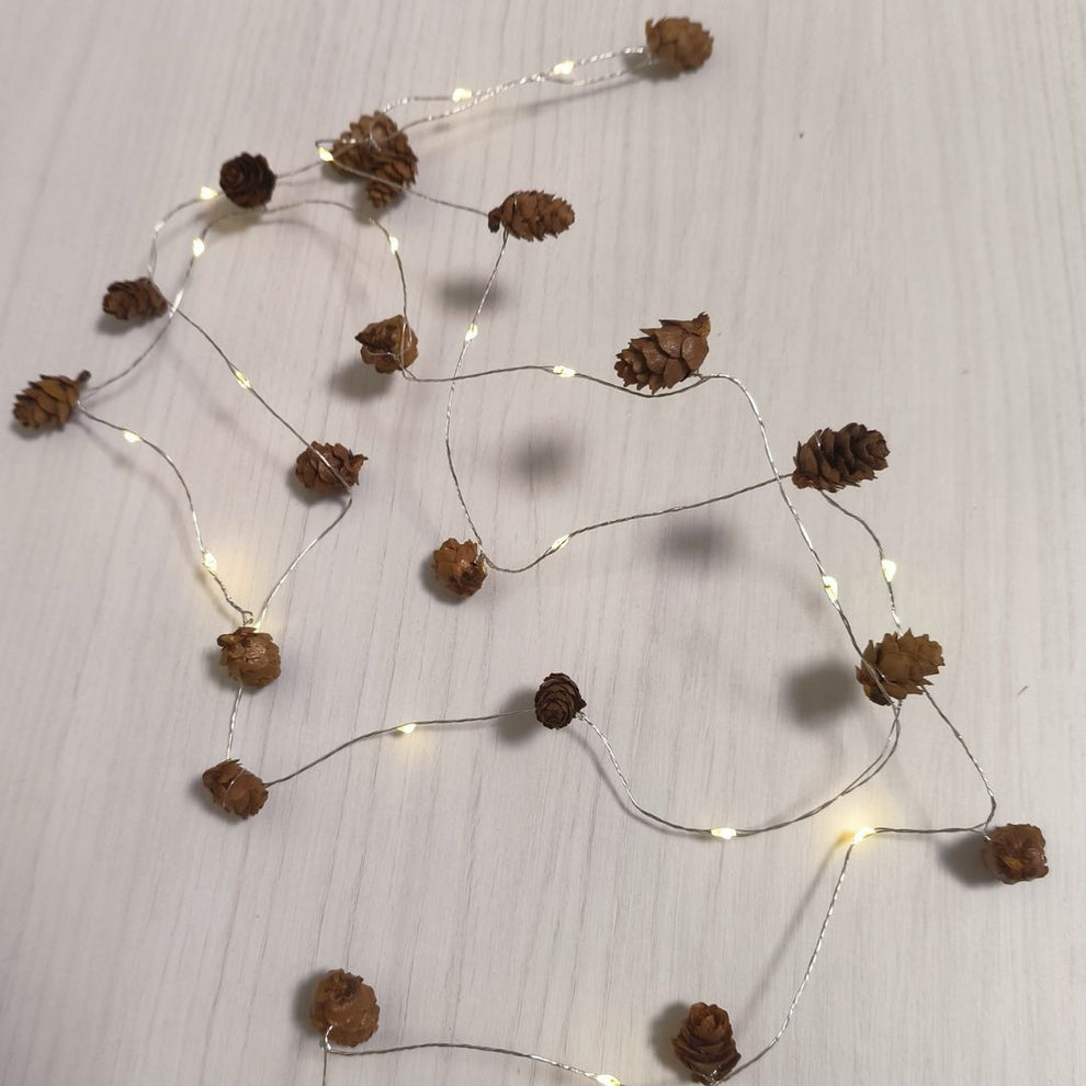 Una cadena de luces con pequeños conos de pino en una superficie de madera blanca.