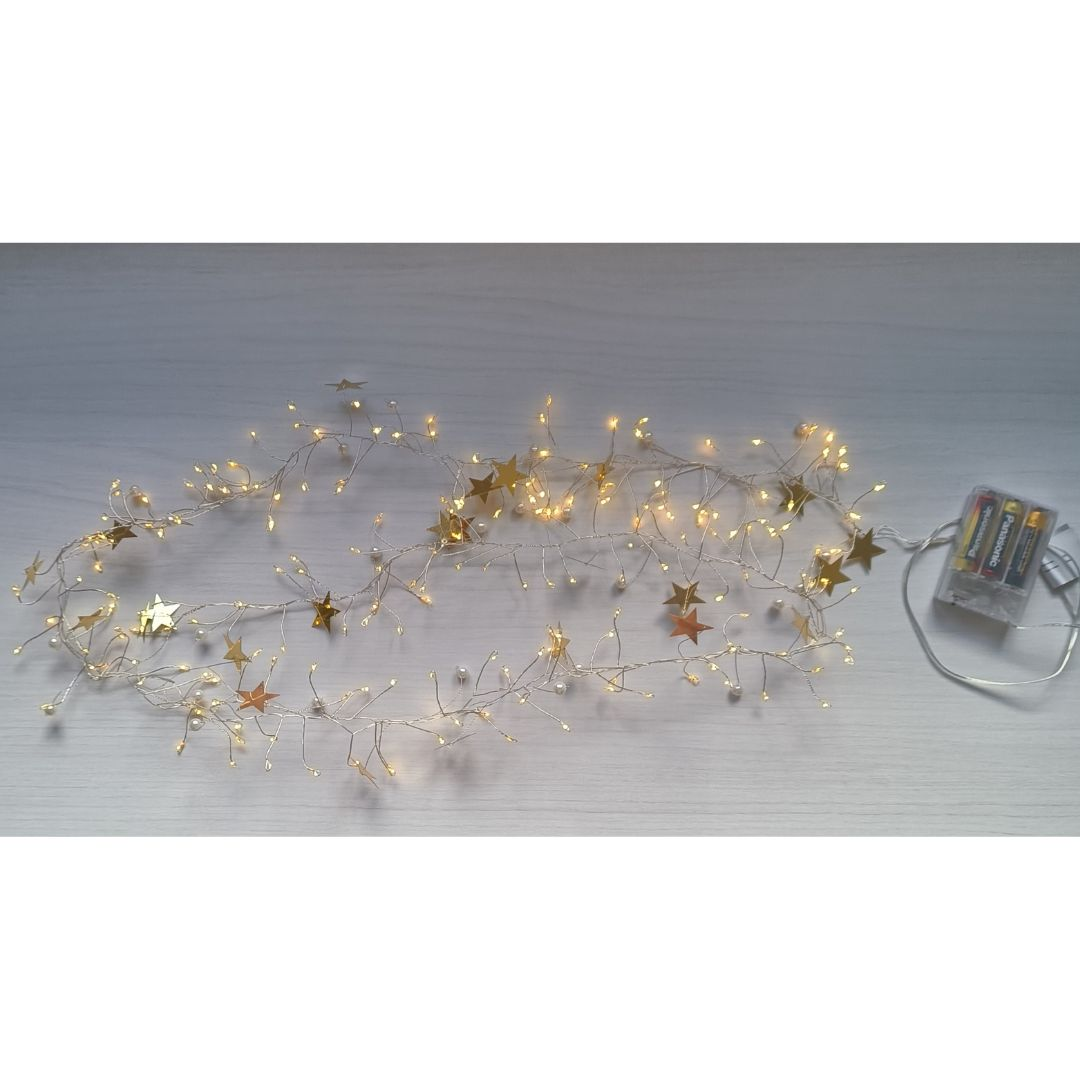 Una cadena de luces con LED cálidos, estrellas doradas y pequeñas perlas sobre una superficie de madera clara.