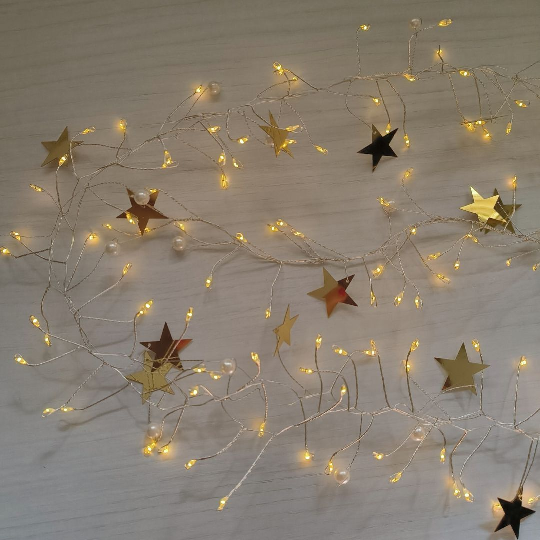 Una cadena de luces cálidas con estrellas doradas y perlas blancas sobre una superficie de madera clara.