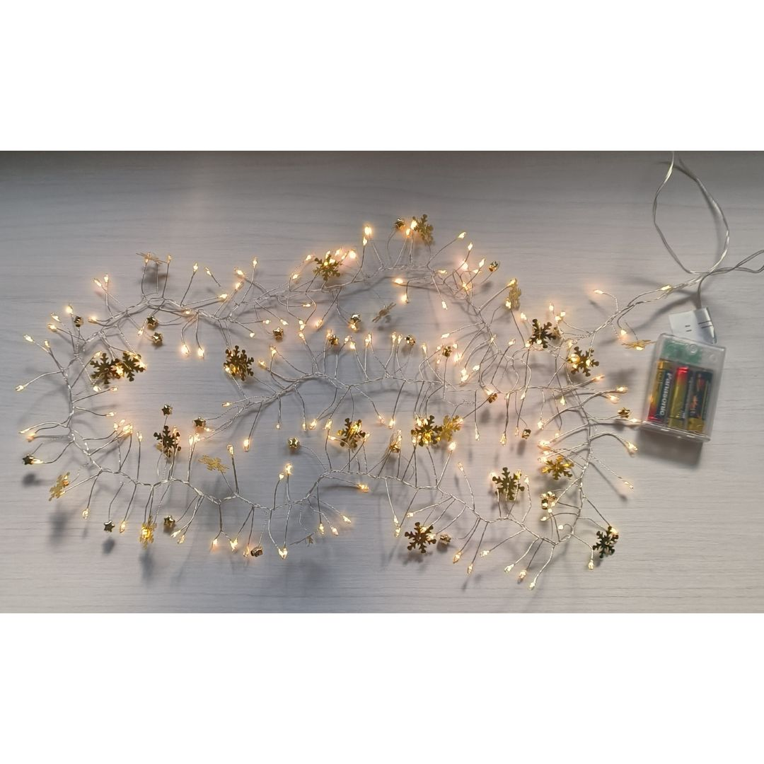 Una cadena de luces blancas cálidas con adornos dorados de copos de nieve se encuentra sobre una superficie de madera clara.