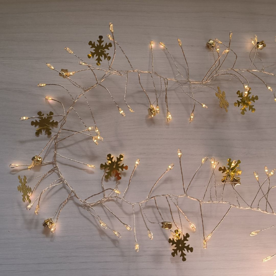 Una cadena de luces LED cálidas con copos de oro sobre fondo de madera clara.
