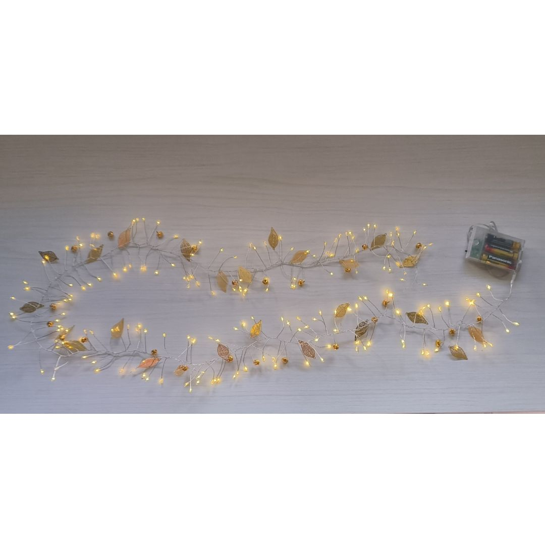 Una guirnalda de luces larga con hojas doradas y pequeñas luces descansa sobre una superficie de madera clara.