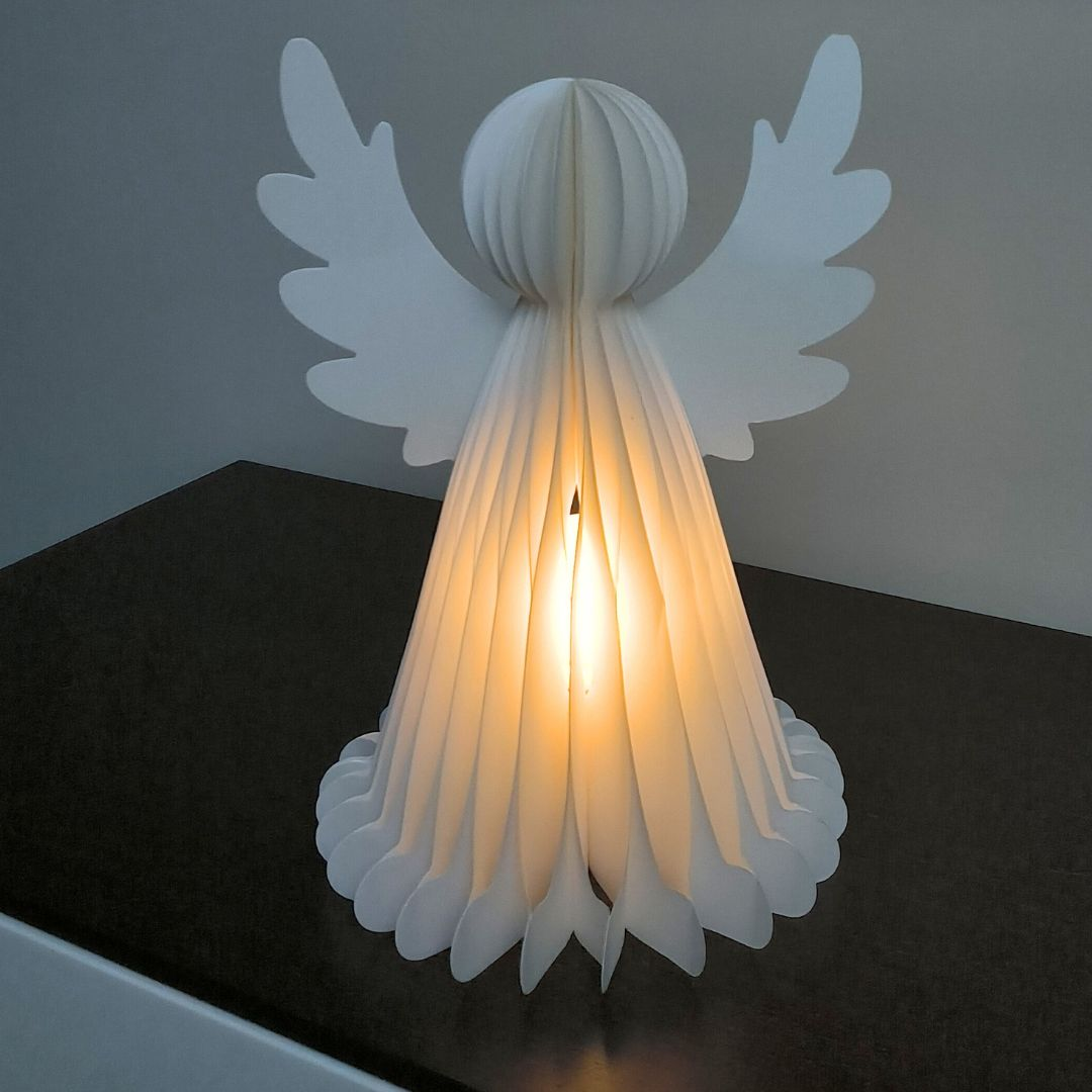 Una lámpara de ángel de papel blanco brilla cálidamente en una superficie oscura.