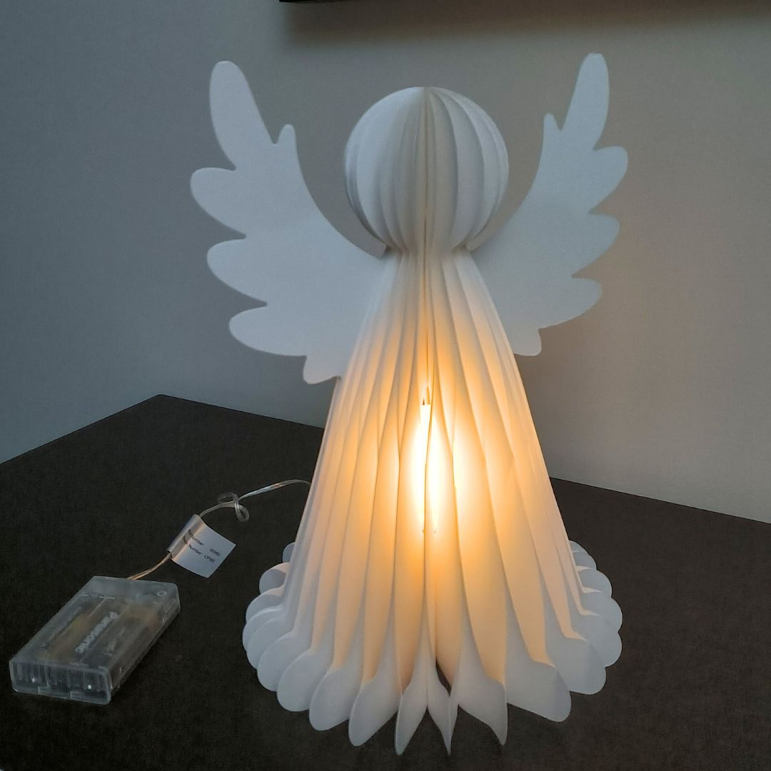 Una lámpara de ángel de papel blanco brilla desde su interior, sobre una superficie oscura.