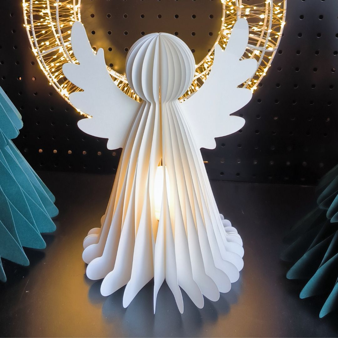 Una figura de ángel blanca de papel con una luz dentro se encuentra frente a luces.