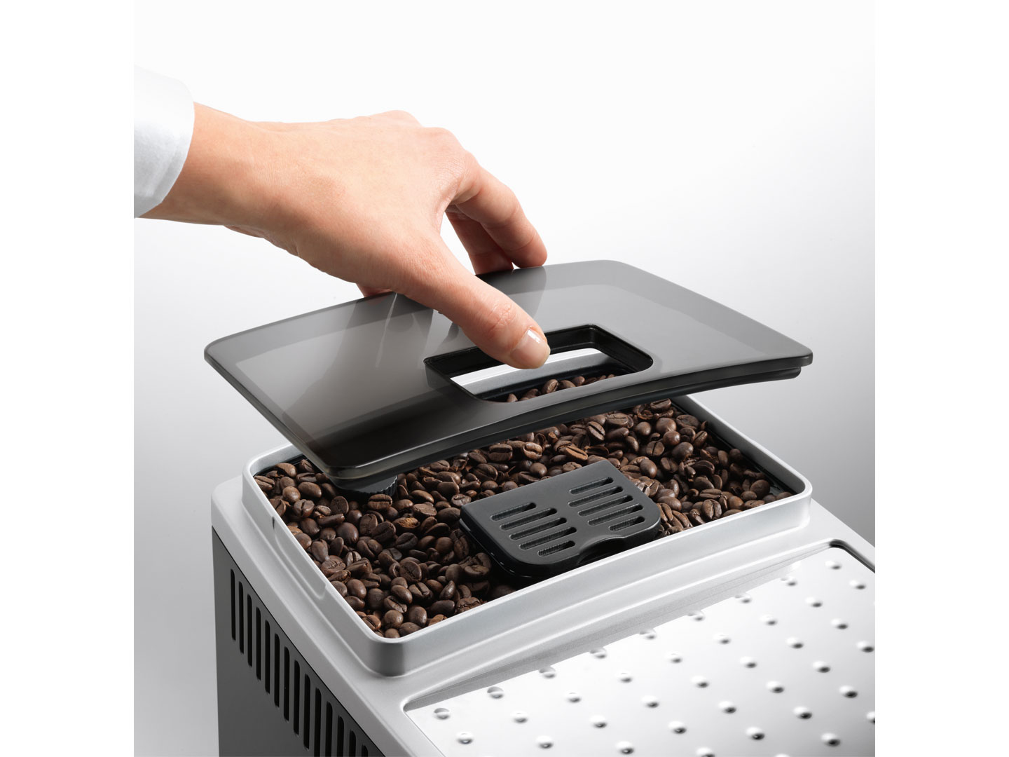 Una mano abre la tapa de un contenedor de granos de café en una máquina.