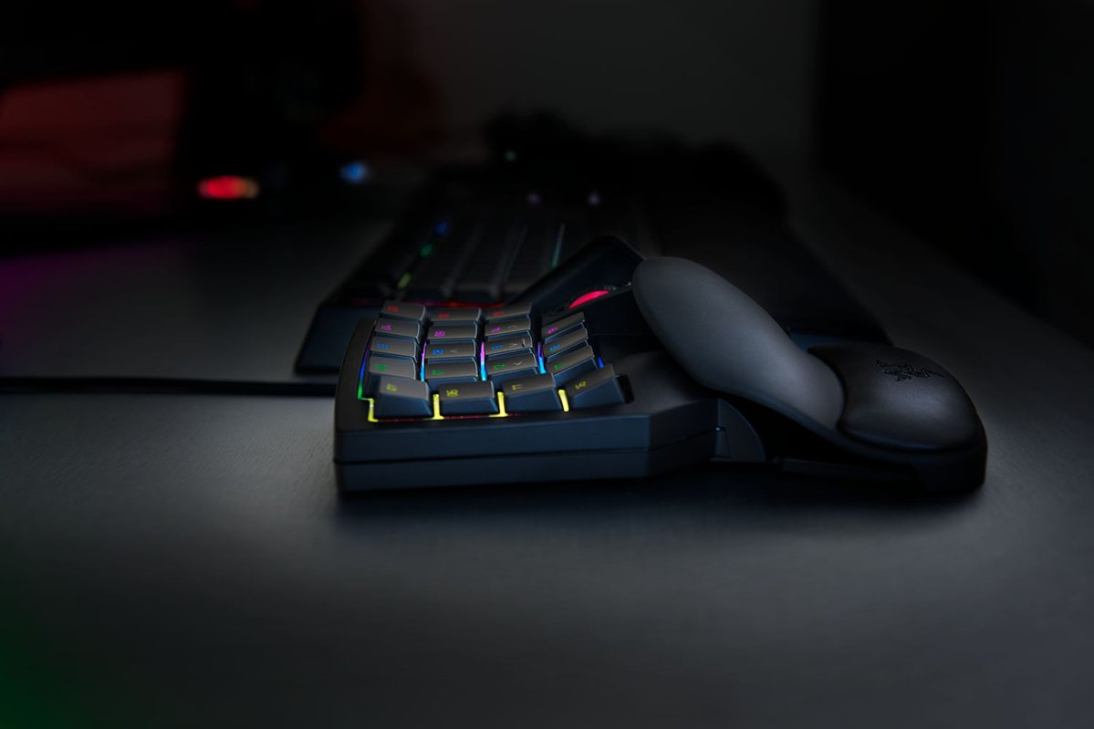 Ein schwarzes Gaming-Keypad mit bunter RGB-Hintergrundbeleuchtung liegt auf einem dunklen Schreibtisch.
