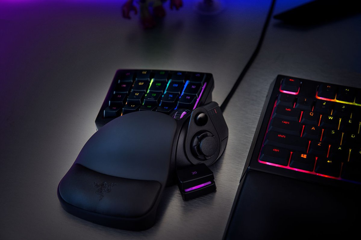 Ein beleuchtetes Gaming-Keypad mit Handballenauflage und eine Tastatur auf einem dunklen Tisch.