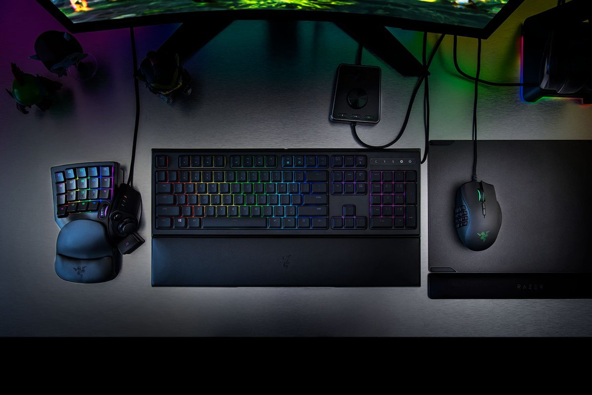 Ein Gaming-Setup mit Tastatur, Maus, Keypad und farbiger Hintergrundbeleuchtung auf einem metallischen Schreibtisch.