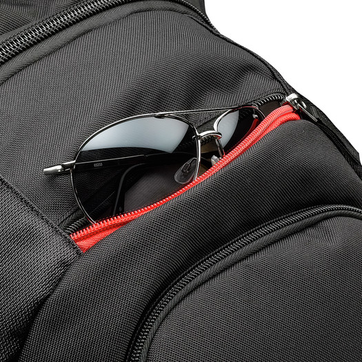 Eine schwarze Sonnenbrille steckt in der teilweise geöffneten roten Reißverschlusstasche eines schwarzen Rucksacks.