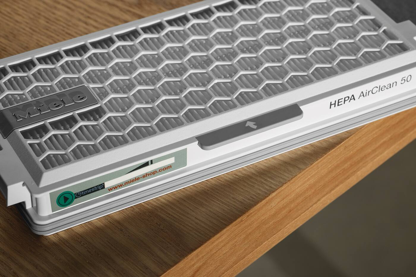 Un filtro Miele HEPA AirClean 50 poggia su una superficie di legno.