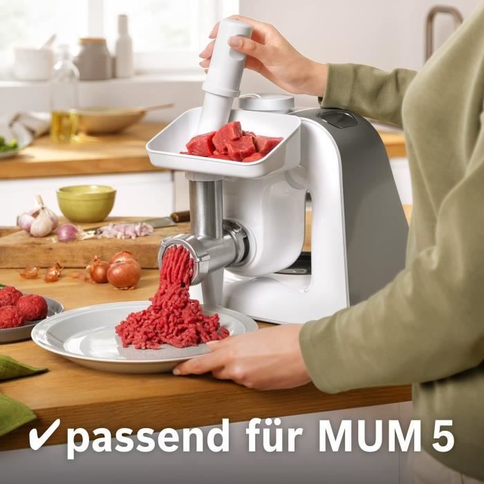 Eine Person benutzt einen weißen Fleischwolf mit rohem Fleisch auf einem Holztisch in einer Küche.