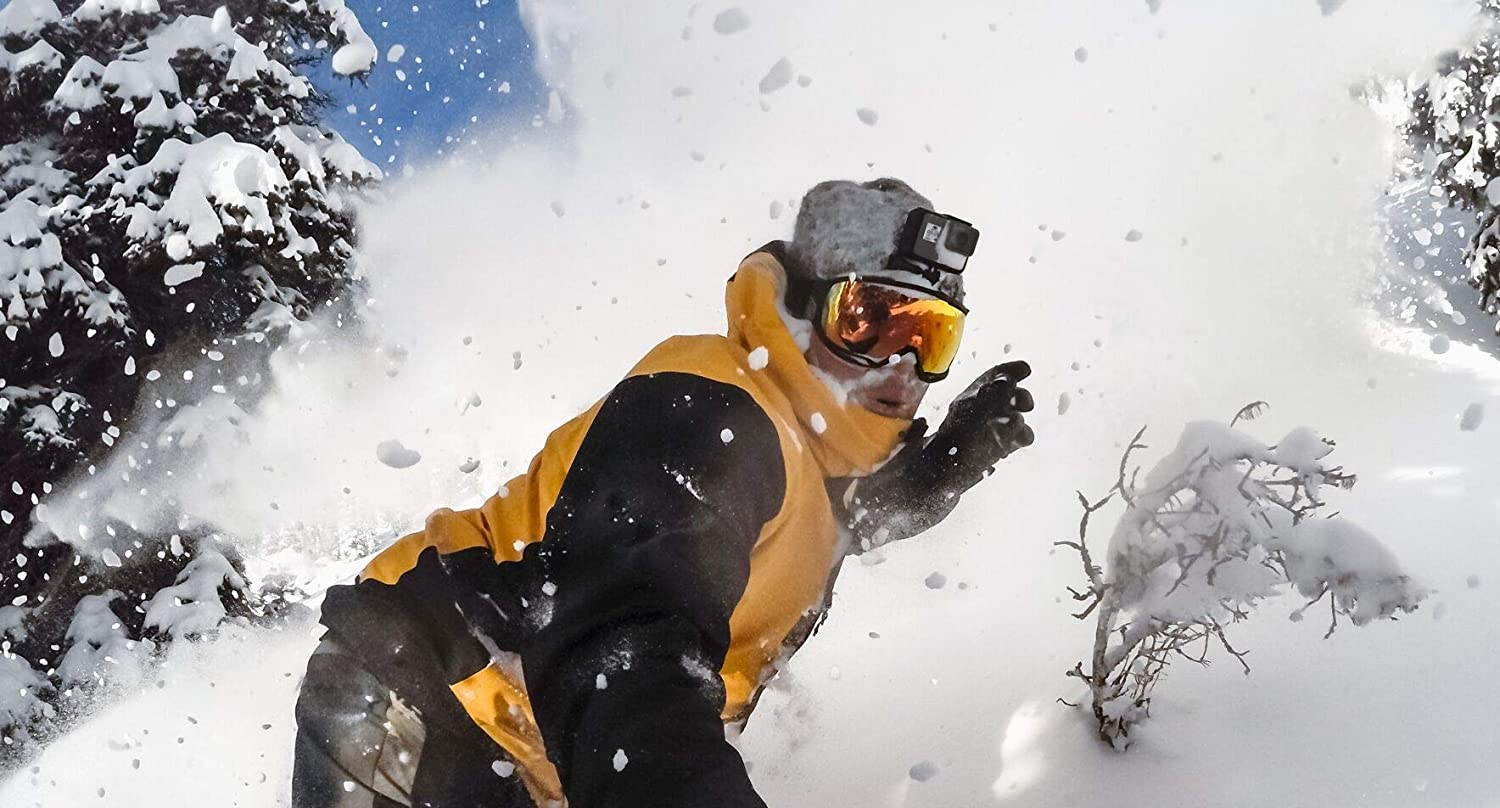 Un esquiador con chaqueta amarilla y gafas levanta nieve en una pendiente nevada.