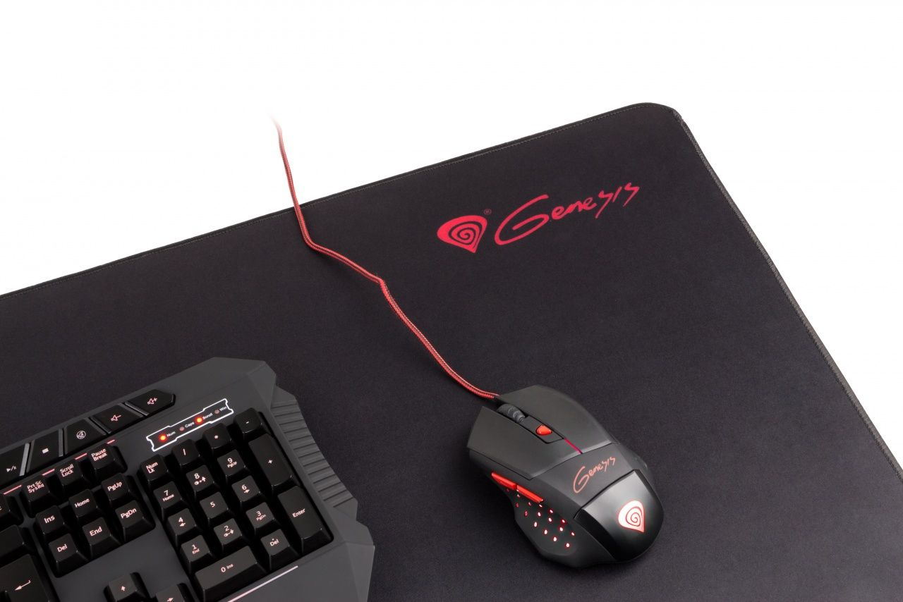 Alfombrilla de ratón Genesis negra con logotipo rojo, un ratón con cable y parte de un teclado.