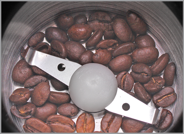 Braune Kaffeebohnen füllen eine Metall-Kaffeemühle mit Zentralklinge.